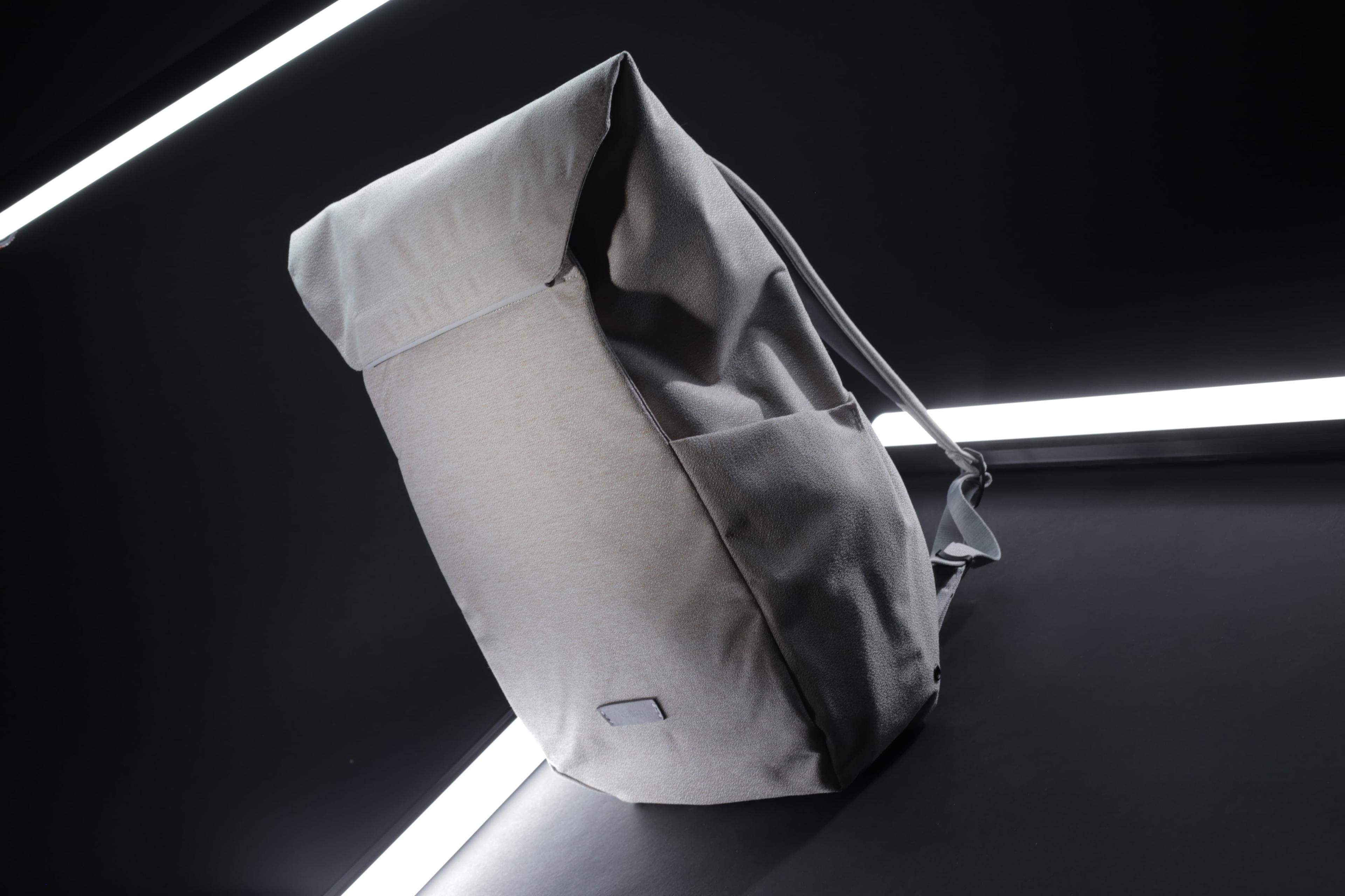 A stylish two-tone backpack positioned upright on a dark surface, illuminated by two diagonal white light strips.