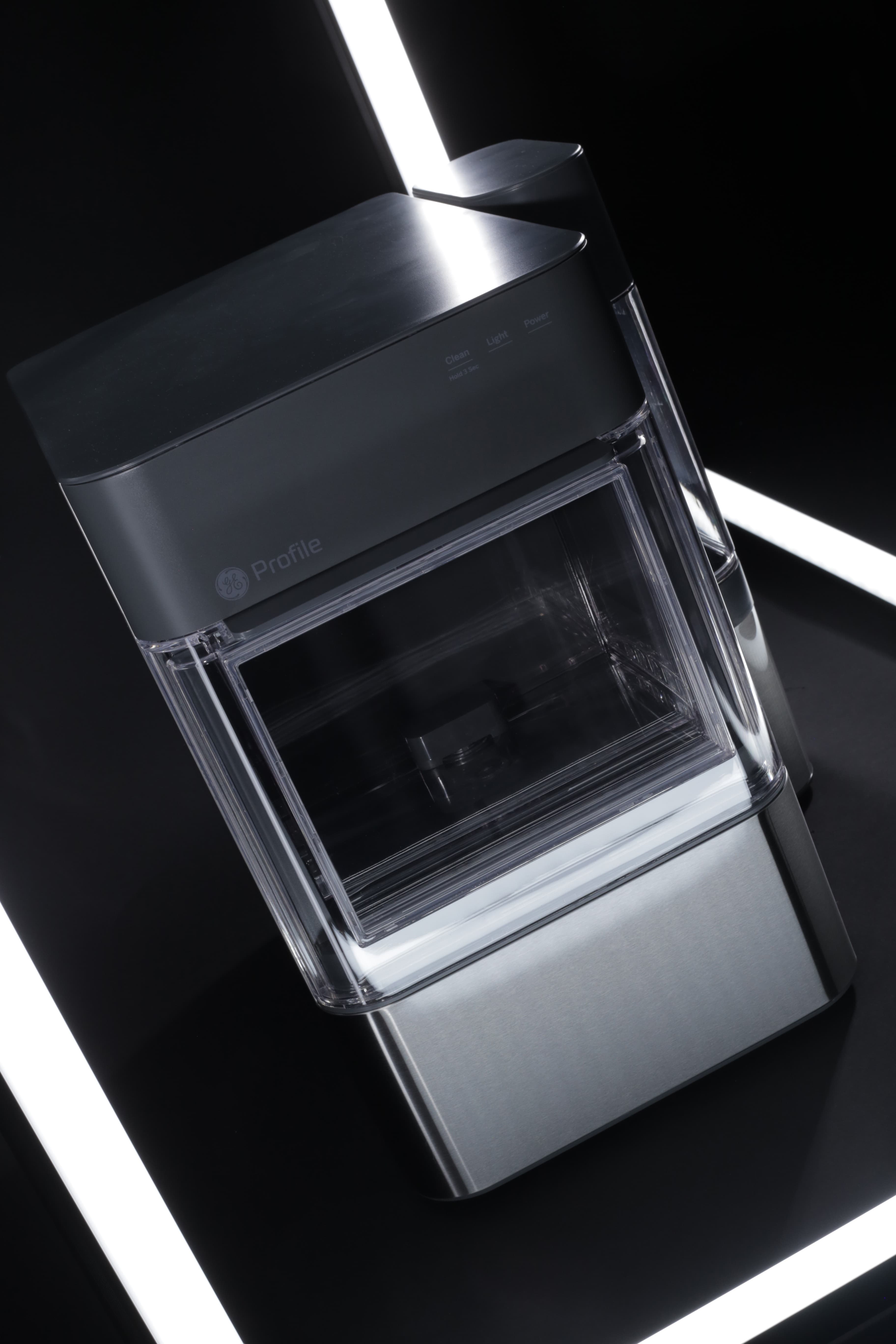 A modern GE Profile ice maker with a transparent ice storage compartment, set against a black background with two white light strips.