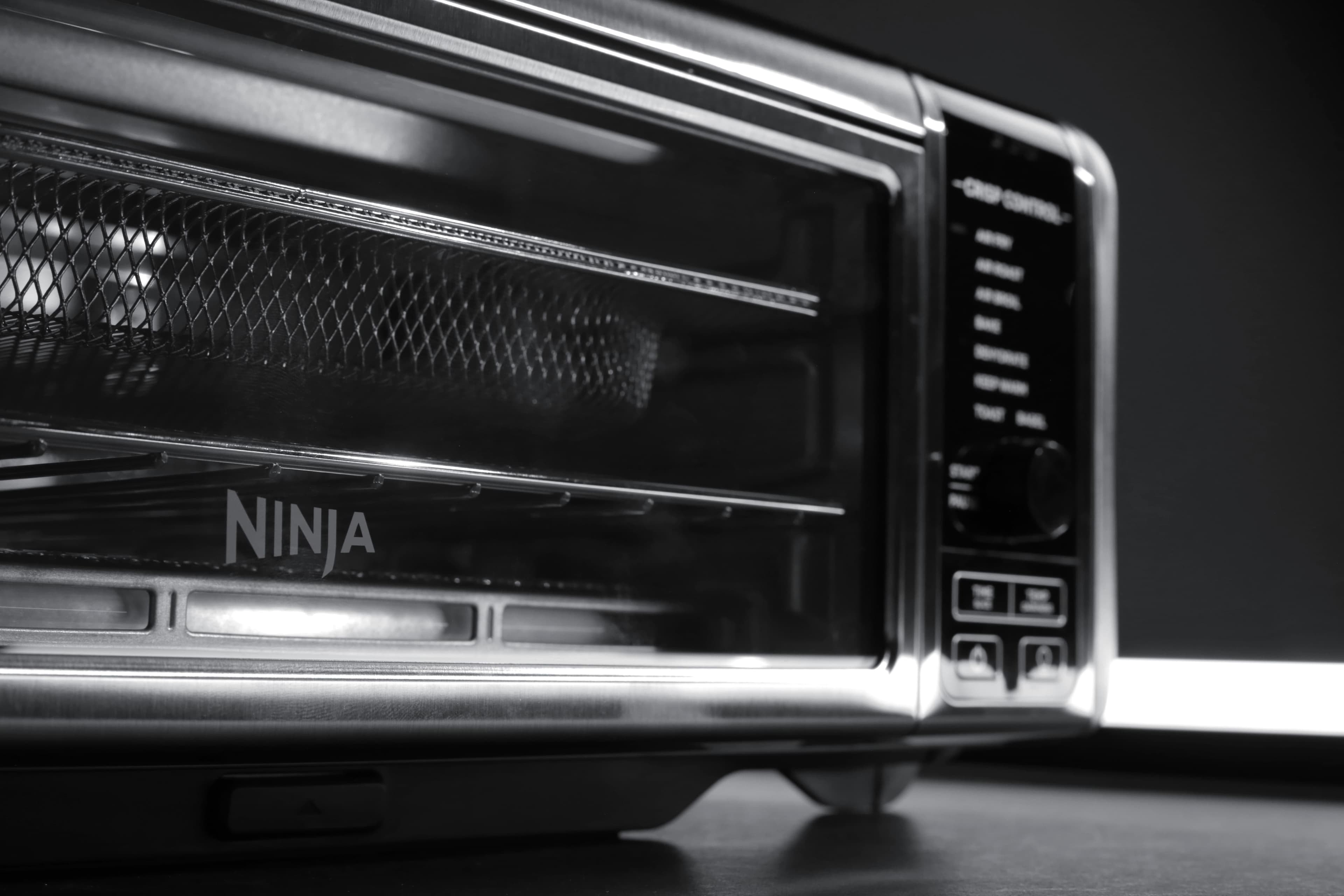 Close-up of a Ninja brand air fryer oven showcasing its interior racks and controls, in a monochrome setting.