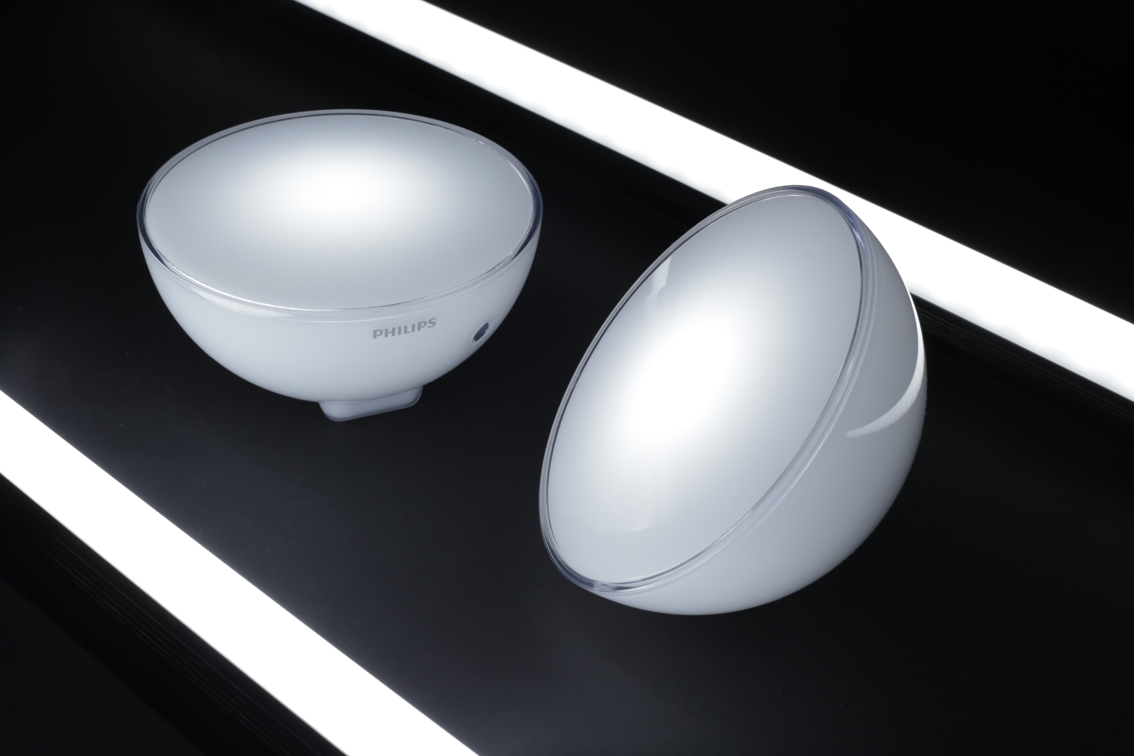 Two Philips dome-shaped, white light therapy devices positioned on a reflective surface, illuminated by parallel white light strips.